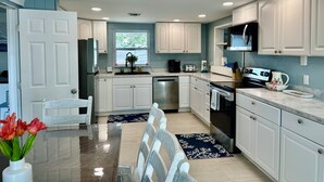 Una cocina moderna con armarios blancos, electrodomésticos de acero inoxidable y un comedor con mesa y sillas de vidrio.