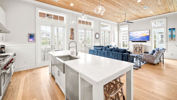 A spacious kitchen with a central island, a dining area with a blue sofa, and a living room with a TV. - Sand Volleyball Court w/ Pool and Views (Santa Rosa Beach)