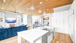 A modern kitchen with white cabinets, a central island, and a dining area with a blue sofa. - Sand Volleyball Court w/ Pool and Views (Santa Rosa Beach)