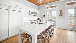 A spacious kitchen with white cabinetry, a large island with bar stools, a stainless steel range hood, and a view to the outside. - Sand Volleyball Court w/ Pool and Views (Santa Rosa Beach)