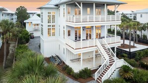 A multi-story coastal house with a balcony, surrounded by palm trees and a driveway. - Sand Volleyball Court w/ Pool and Views (Santa Rosa Beach)
