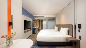 Een moderne hotelkamer met een groot bed, een televisie, een bureau en een badkamer in de achtergrond.