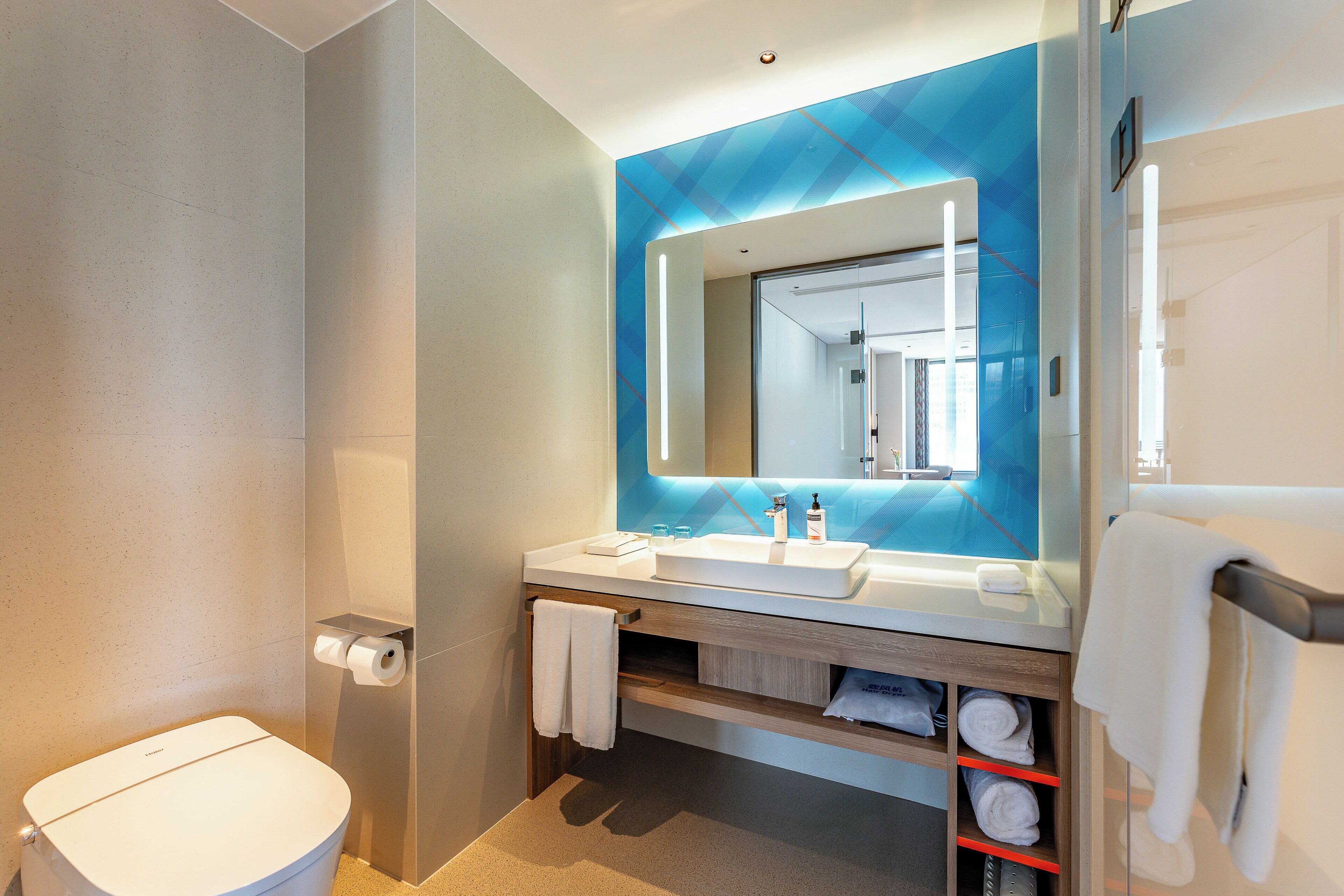 Un baño moderno con inodoro blanco, lavamanos con espejo y perchero.