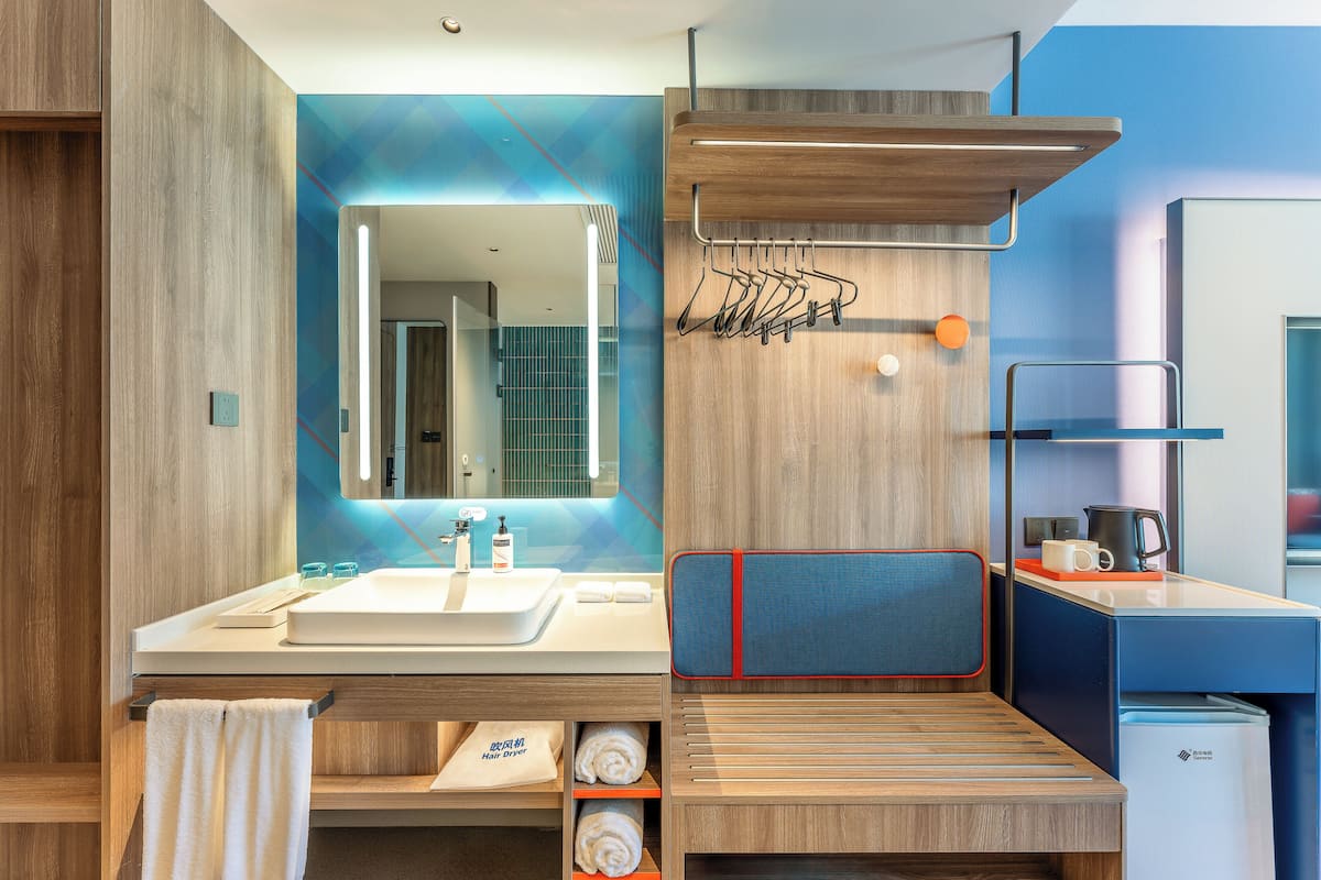 A modern bathroom with a wooden vanity, a mirror, a towel rack, and a small seating area.