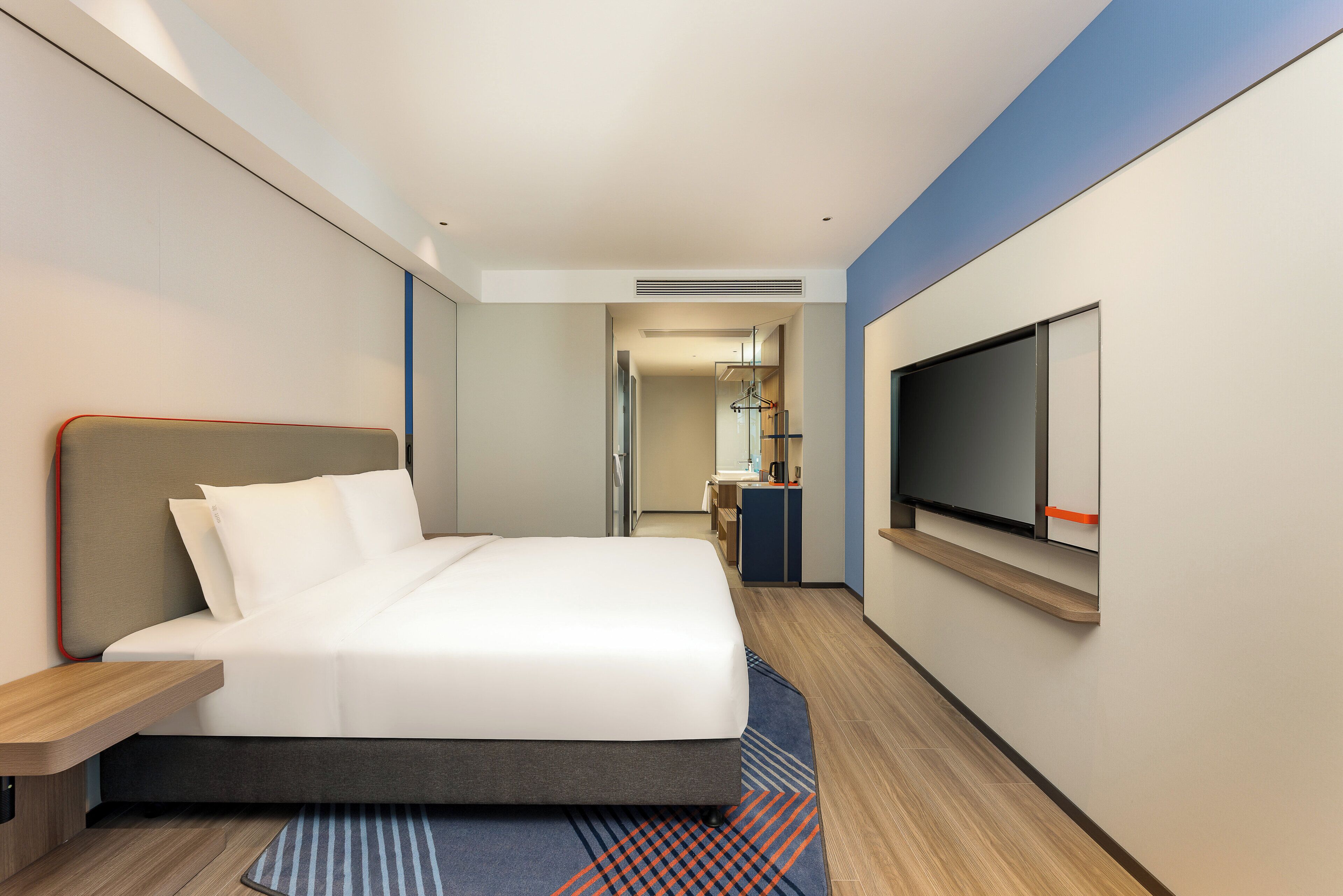 Una habitación de hotel moderna con una cama grande, un televisor montado en la pared y un escritorio pequeño.