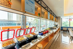 Zona de bufé con diferentes recipientes de comida y un área de descanso con vista a la ciudad.