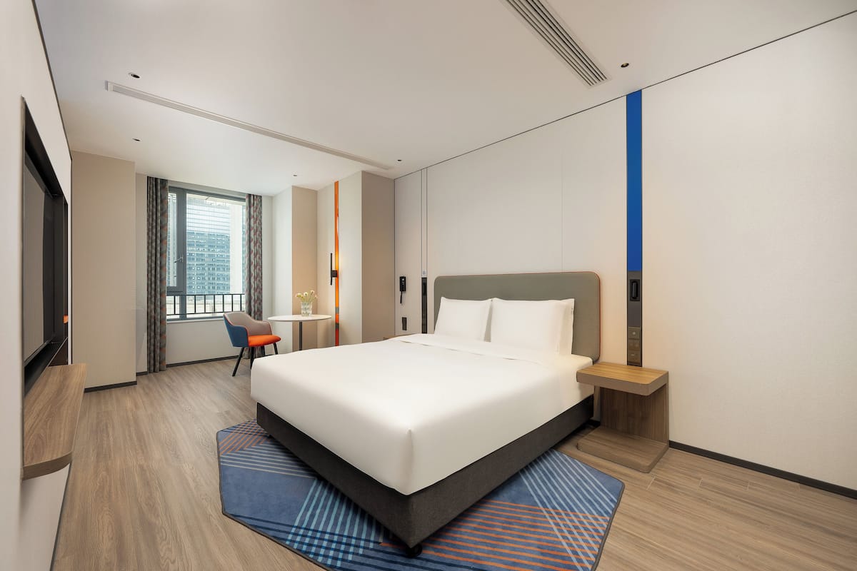 A modern hotel room with a large bed, a desk, and a chair.