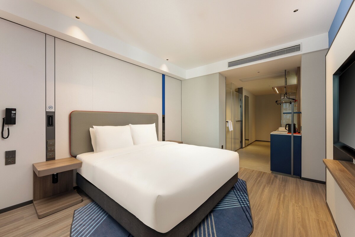 Una habitación de hotel moderna con una cama grande, una mesita de noche, un escritorio integrado y un televisor.