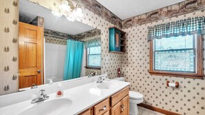 A bathroom with a large mirror, two sinks, wooden cabinets, a toilet, and a window with a view.