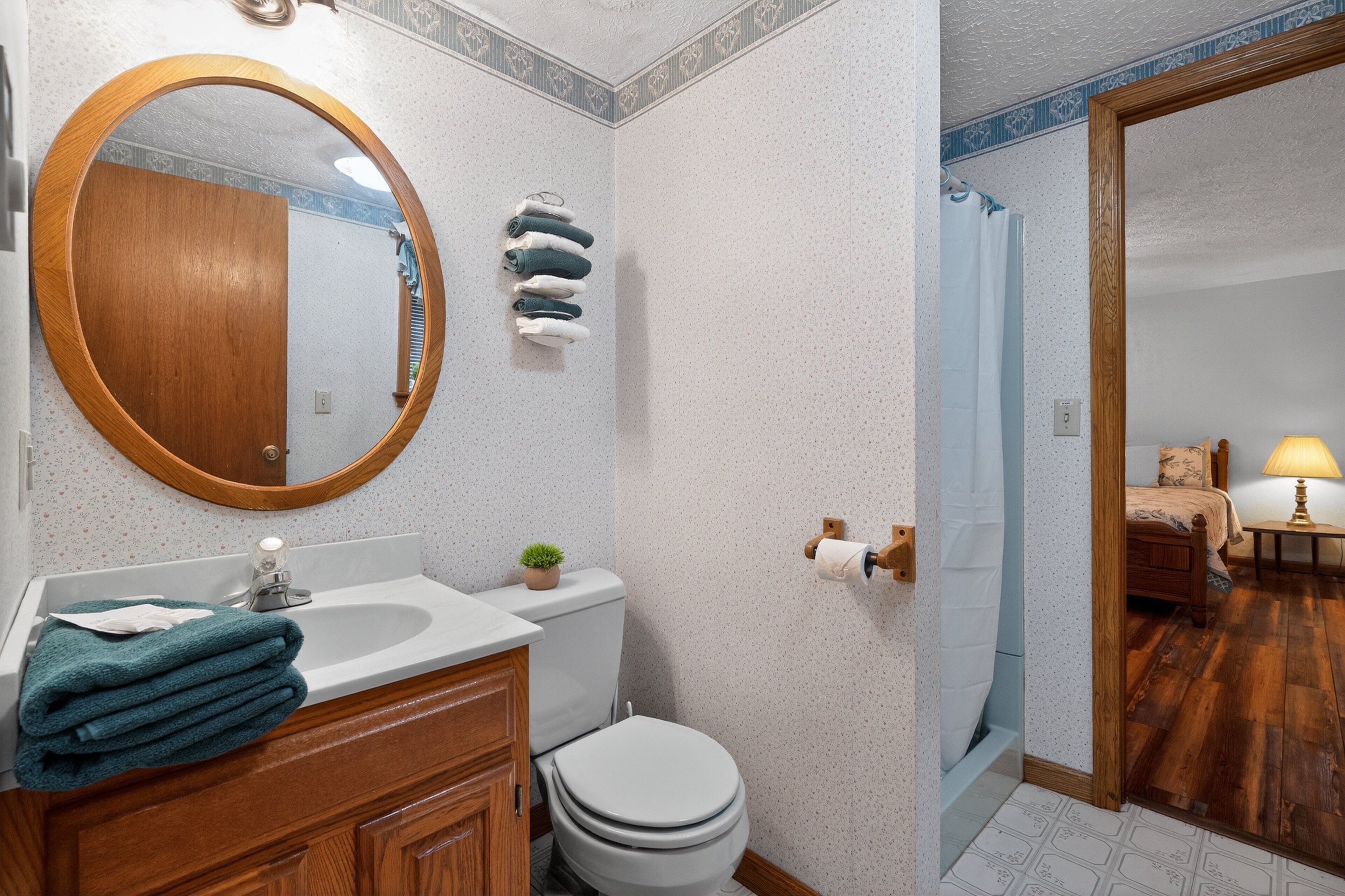 A bathroom with a wooden vanity, a round mirror, a toilet, and a shower area.