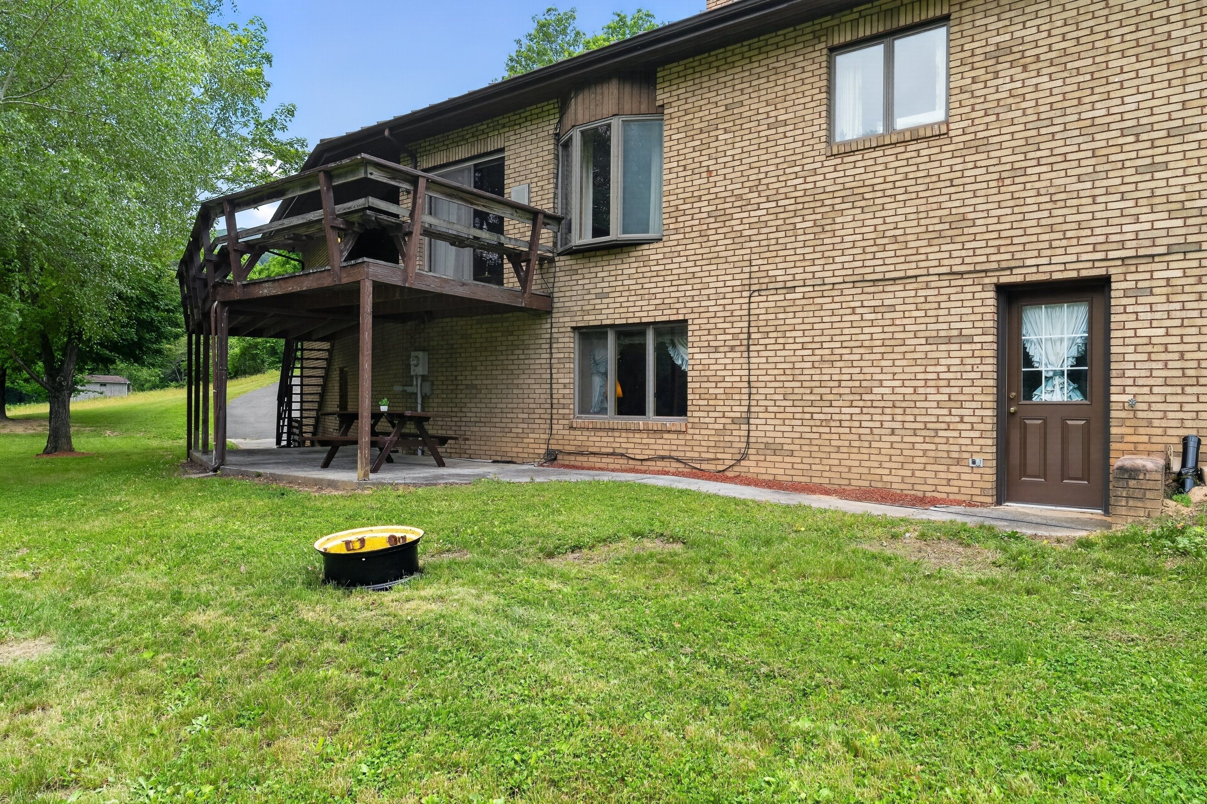 A two-story brick building with a wooden deck, a picnic table, and a black trash bin in the yard.