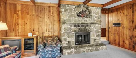 Une pièce chaleureuse avec une cheminée en pierre, des murs en bois, un canapé et un téléviseur.