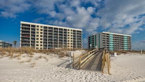 Ett hotell vid stranden med flera våningar, en sandstrand i förgrunden och en klar himmel.