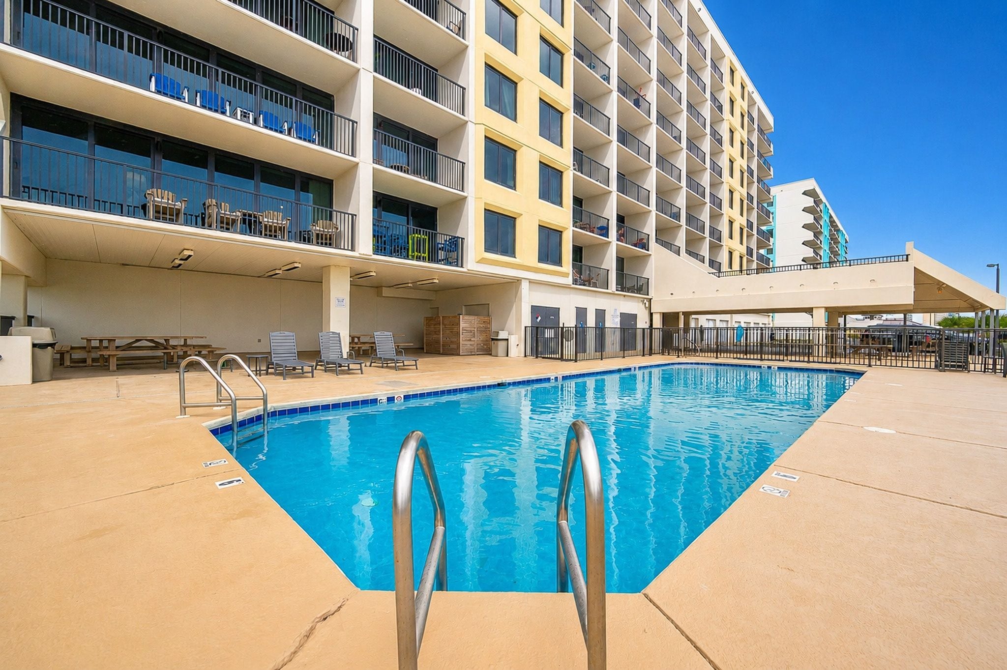 Un área de piscina de hotel con piscina azul cristalina, sillas de descanso y un edificio de varios pisos con balcones.