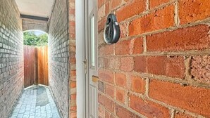 Um corredor de tijolos estreito, com uma porta à direita e uma janela no final.