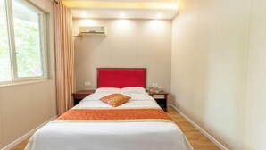 Een hotelkamer met een enkel bed, een rode hoofdbord, een nachtkastje en een airconditioner aan de muur.