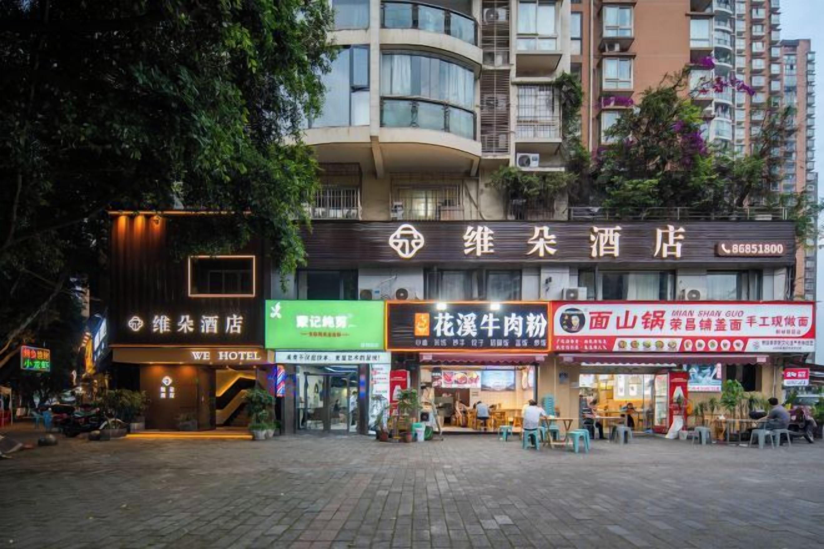 A hotel with a modern facade, multiple signage, and a paved outdoor area with seating.