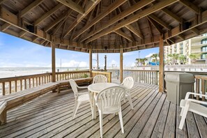 Een houten terras met witte kunststof stoelen en een tafel, met uitzicht op het strand.
