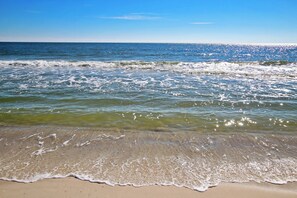 Een strand met helder water en golven, een zandstrand en een blauwe lucht.