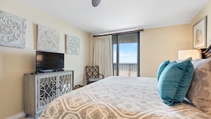 Une chambre avec un grand lit, un téléviseur posé sur un meuble et une vue à travers une porte coulissante.
