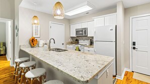 A modern kitchen with a granite countertop, white cabinetry, stainless steel appliances, and a bar stool area.
