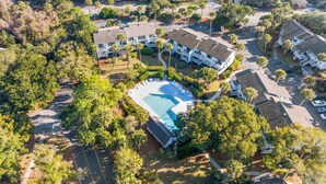 An aerial view of a residential area with multiple two-story houses, a swimming pool, and lush greenery.