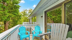 A wooden deck with two turquoise Adirondack chairs and a bench, overlooking a lush green landscape.