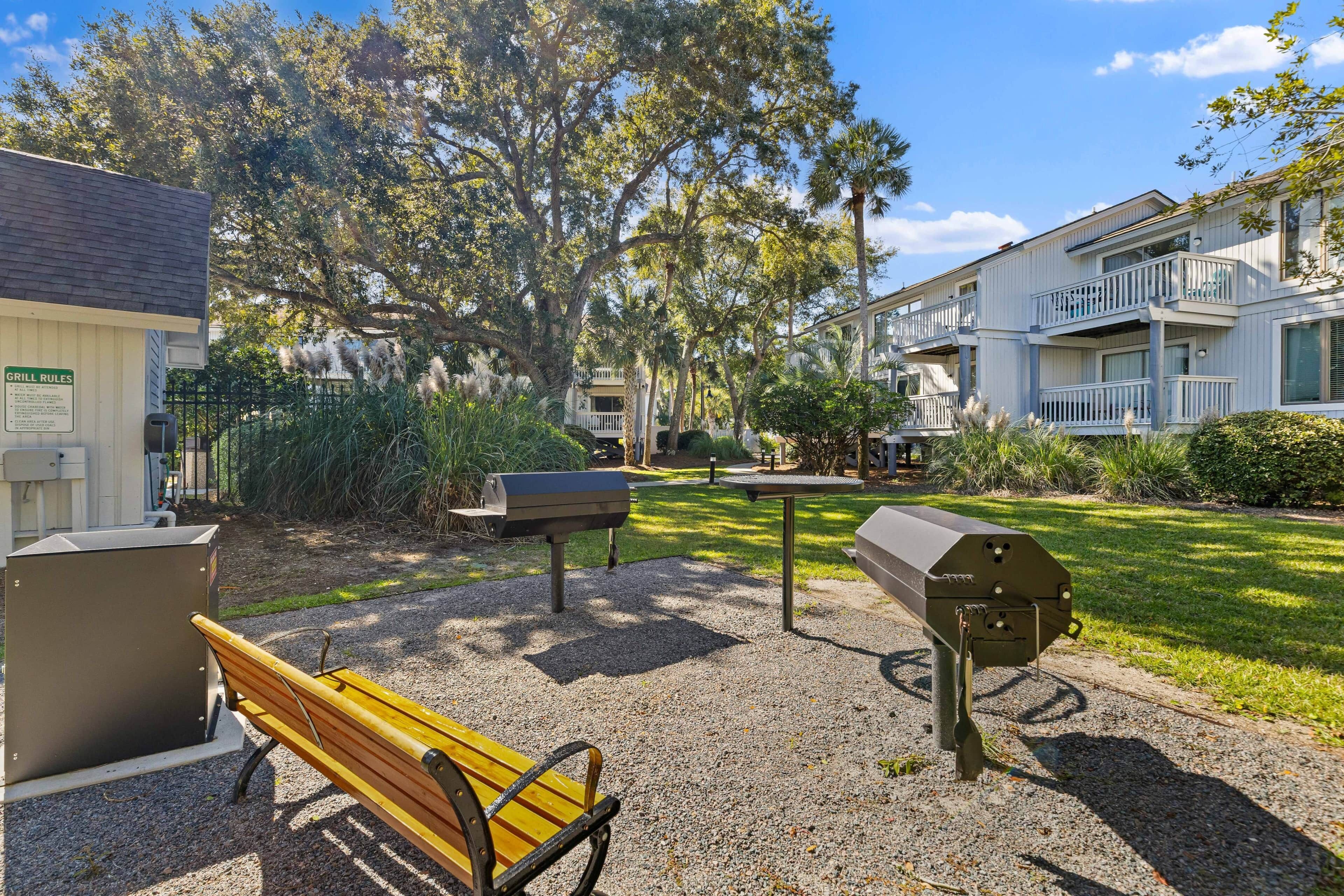 A park area with a bench, barbecue grills, and a building with balconies.
