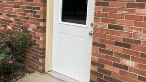 A white door with a window, set in a brick wall.
