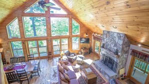Ein geräumiges Chalet mit hohen Decken, großen Fenstern, einem Kamin aus Stein und einer gemütlichen Sitzecke.