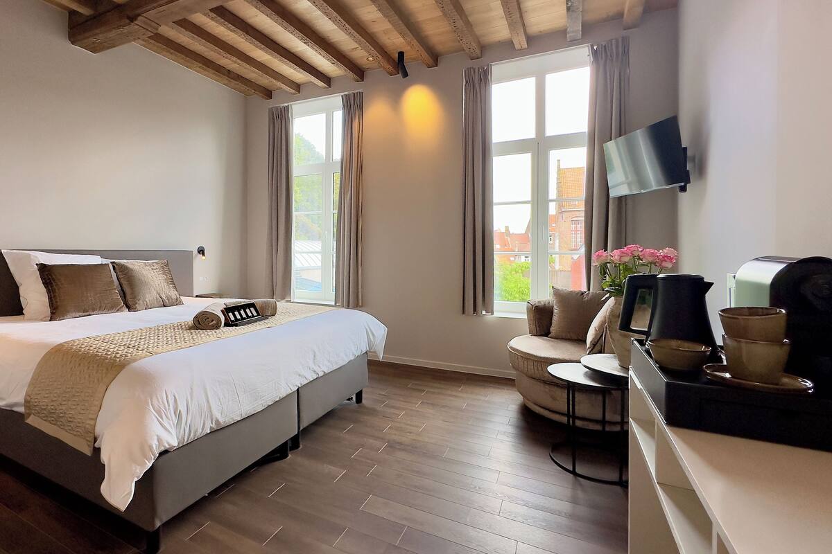 A bedroom with a bed, a desk with a chair, a TV, and a window with curtains.