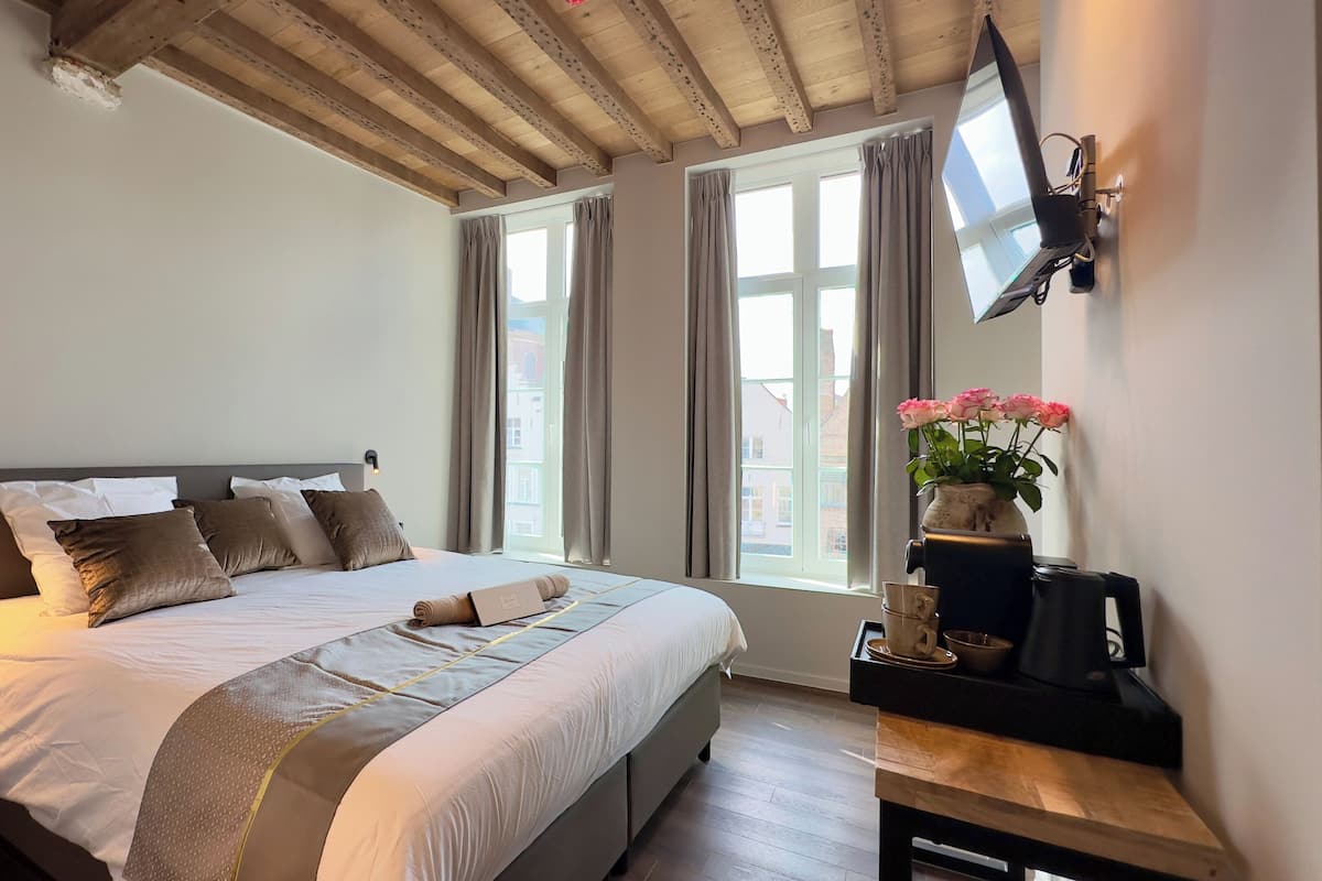 A bedroom with a bed, a bedside table, a TV mounted on the wall, and a window with curtains.