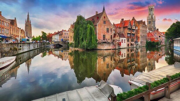 Un canal con edificios reflejados en el agua, un puente y una torre.