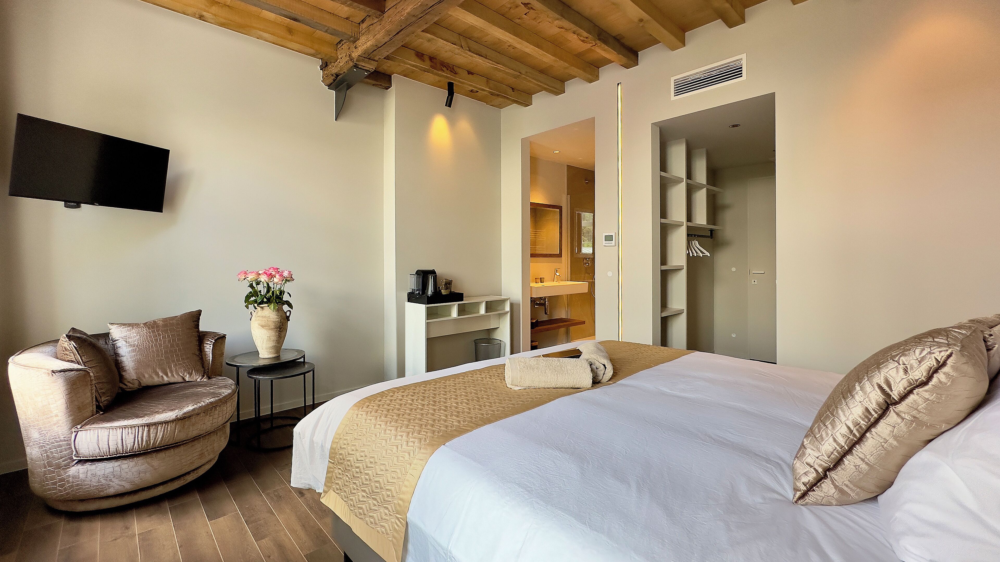 A bedroom with a large bed, a chair, a small table with a vase of flowers, and a built-in wardrobe.
