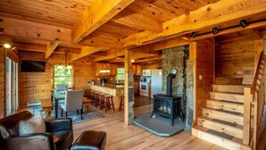 A wooden cabin interior with a living room, kitchen, and a stone fireplace. - Spacious Log Home Overlooking 40 White Mnt Peaks with Extreme Privacy: Host Weddings (Brownfield)