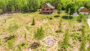 A large log cabin with a wrap-around porch, surrounded by a forested landscape and hills in the background. - Spacious Log Home Overlooking 40 White Mnt Peaks with Extreme Privacy: Host Weddings (Brownfield)