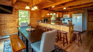 A wooden cabin with a kitchen featuring a central island, bar stools, and a dining table. - Spacious Log Home Overlooking 40 White Mnt Peaks with Extreme Privacy: Host Weddings (Brownfield)