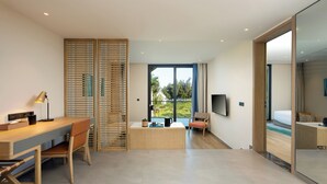 Ein modernes Hotelzimmer mit Schreibtisch aus Holz, einem Sessel, einem Bett, einem Fernseher und einem großen Fenster mit Blick ins Freie.