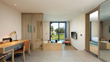 A modern hotel room with a wooden desk, a chair, a bed, a TV, and a large window offering a view of the outdoors.