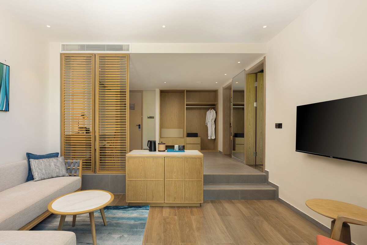 Een moderne hotelkamer met een bank, een klein rond tafeltje, een houten kast en een flatscreen televisie.