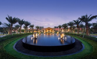 A hotel with a central fountain, palm trees, and a well-maintained lawn.
