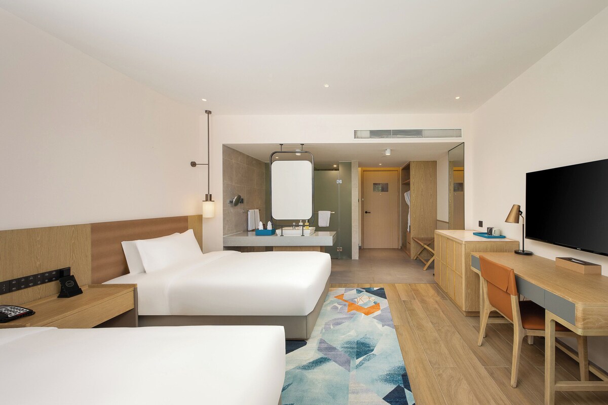 Een hotelkamer met twee bedden, een bureau, een televisie en een badkamer.