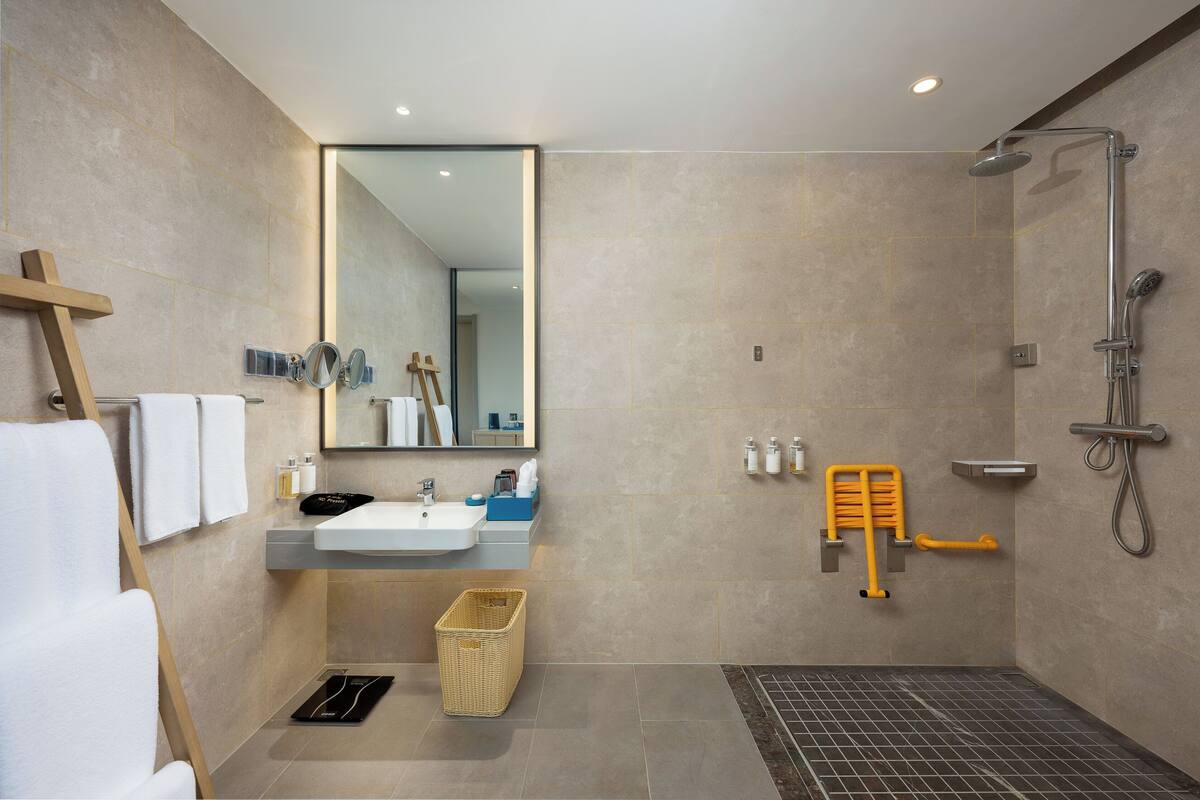 Un baño moderno con lavabo, espejo, ducha y toallero.
