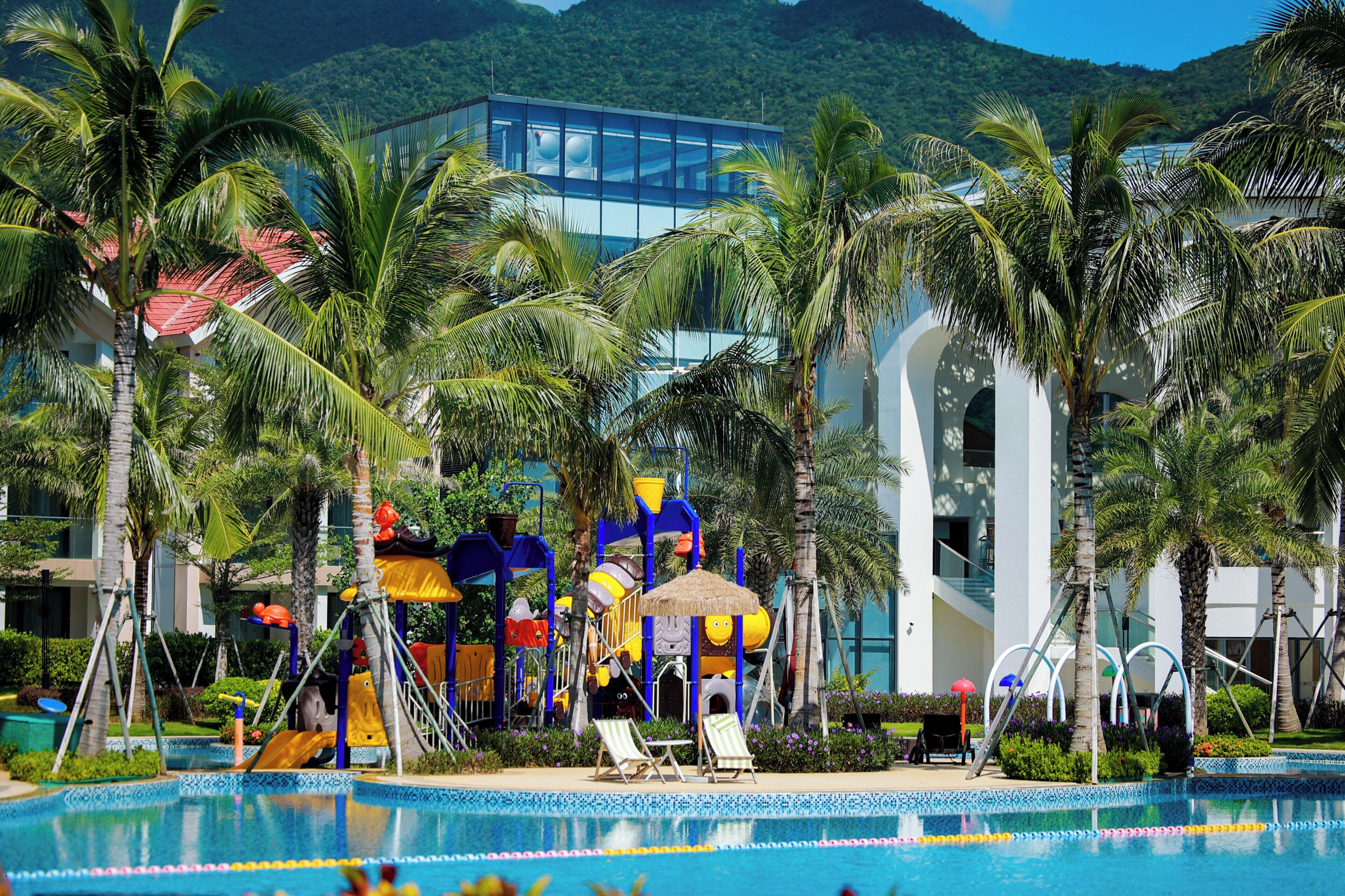 Una piscina con tobogán, palmeras y un edificio moderno al fondo.