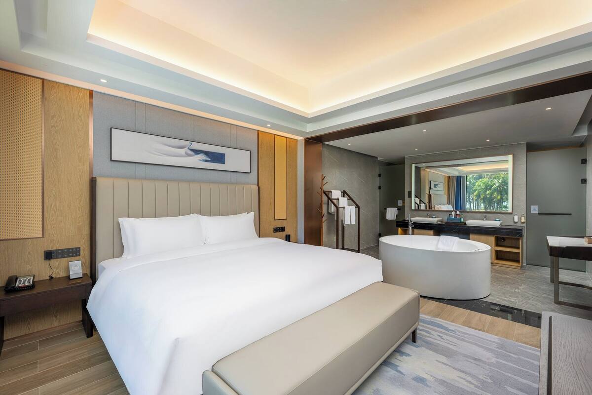 Una habitación de hotel moderna con una cama grande, un área de descanso, una bañera y un baño con un espejo amplio.
