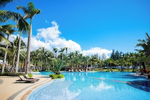 A resort pool area with palm trees, lounge chairs, and a clear blue sky.