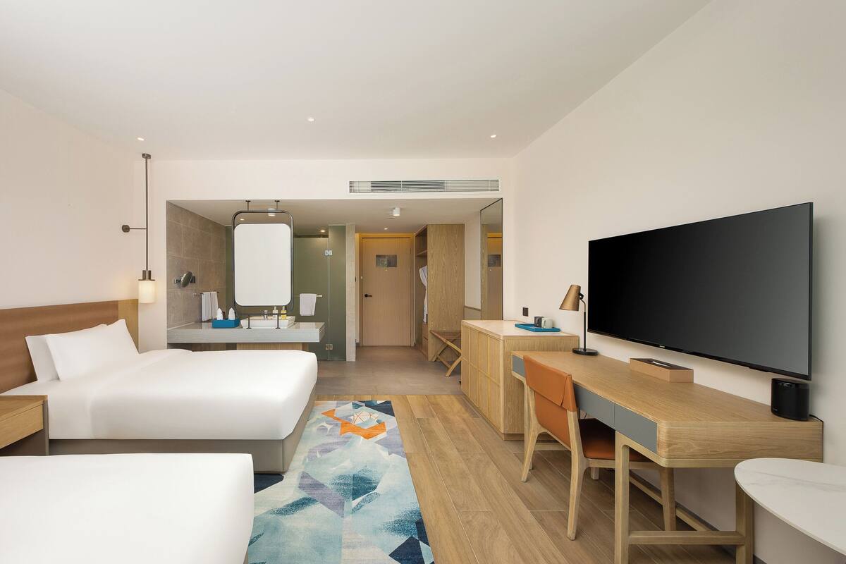 Habitación de hotel con dos camas, un escritorio, televisión y baño.