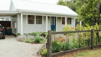 A small, single-story building with a white exterior and a blue door, surrounded by a gravel driveway and a wooden fence.