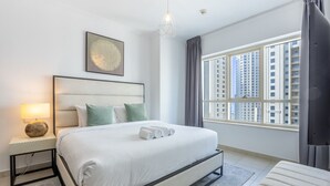 Een moderne hotelkamer met een groot bed, een nachtkastje met een lamp, een kunstwerk in een lijst boven het bed en een uitzicht op wolkenkrabbers door het raam.