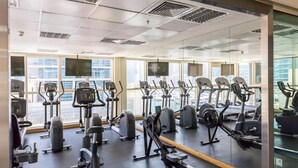 Een sportschool met diverse fitnessapparaten, grote ramen en een spiegelwand.